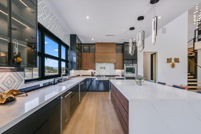 Kitchen featuring modern cabinetry, tasteful tile backsplash, light wood flooring, stainless steel appliances, and glass insert cabinets | Image 17