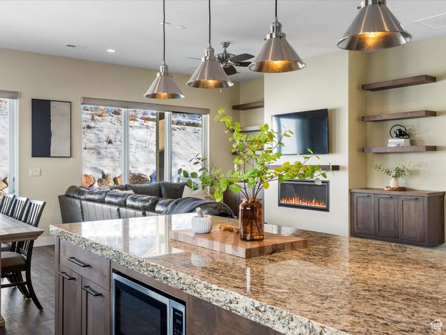 Kitchen with a glass covered fireplace, plenty of natural light, stainless steel microwave, hanging light fixtures, and recessed lighting | Image 7