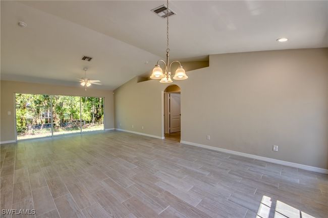 Empty room with arched walkways, lofted ceiling, ceiling fan with notable chandelier, visible vents, and light wood-style floors | Image 14