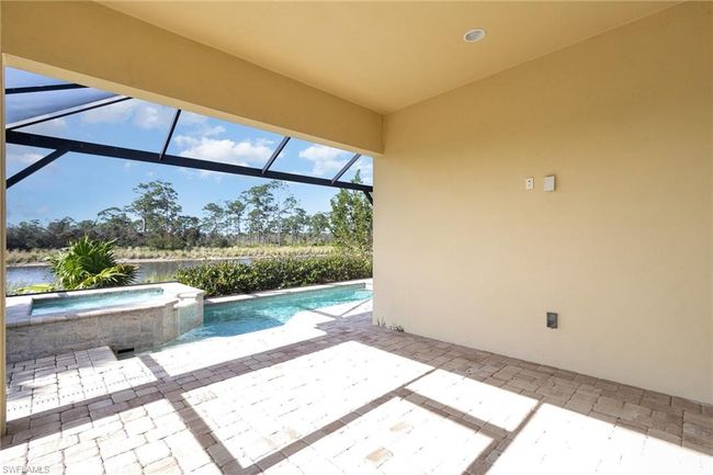 View of patio featuring glass enclosure, a swimming pool with hot tub, and a water view | Image 15