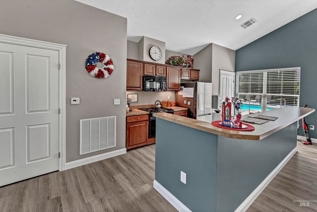 Kitchen with black appliances, light wood finished floors, high vaulted ceiling, light countertops, and a center island | Image 26