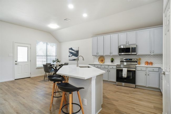 Kitchen featuring appliances with stainless steel finishes, a sink, vaulted ceiling, backsplash, and a breakfast bar | Image 5