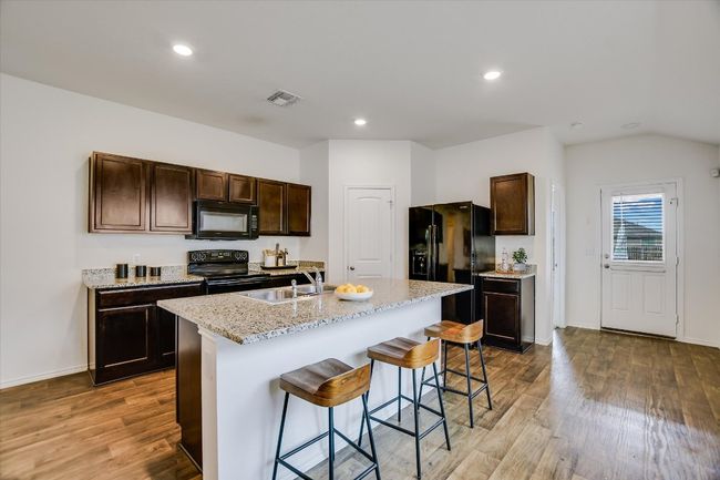 Kitchen with a kitchen breakfast bar, dark brown cabinetry, wood finished floors, a sink, and black appliances | Image 10