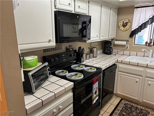 Kitchen featuring black appliances, tile countertops, white cabinets, and light tile patterned floors | Image 14