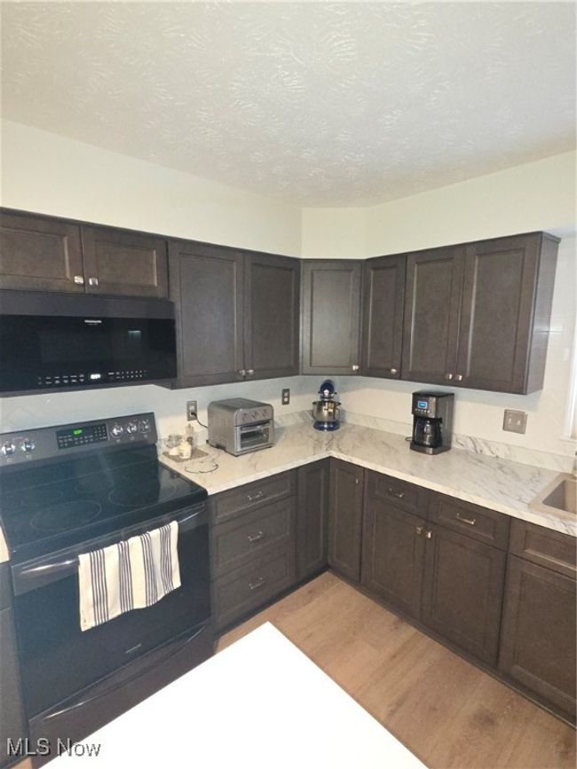 Kitchen featuring range, light wood-style flooring, a textured ceiling, dark brown cabinets, and a toaster | Image 10