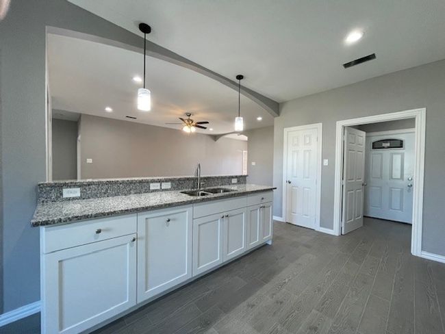 Kitchen with white cabinets, granite counters, ceramic wood-look flooring, decorative light fixtures, and a sink | Image 9