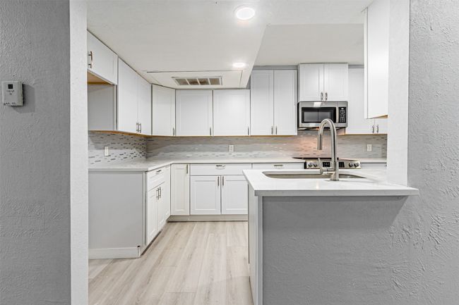 Kitchen with decorative backsplash, kitchen peninsula, white cabinets, and light wood-type flooring | Image 16