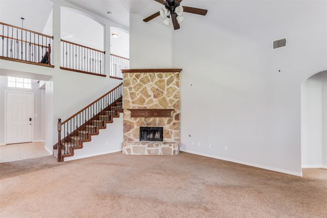 Unfurnished living room featuring a high ceiling, carpet flooring, a ceiling fan, arched walkways, and stairway | Image 8