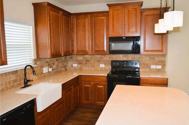 Kitchen with black appliances, a sink, light countertops, decorative backsplash, and dark wood finished floors | Image 4