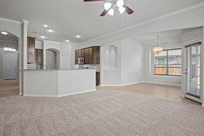 Unfurnished living room with ornamental molding, light carpet, arched walkways, ceiling fan with notable chandelier, and light tile patterned floors | Image 10