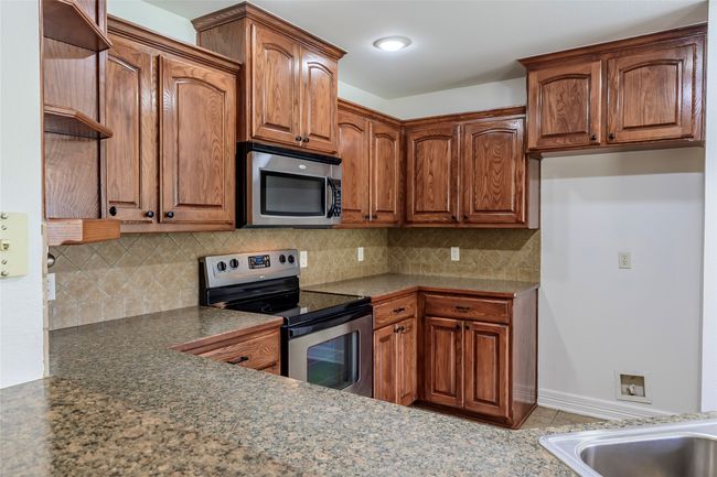 Kitchen with brown cabinetry, appliances with stainless steel finishes, and tasteful backsplash | Image 18