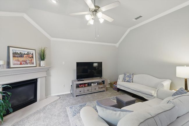 Living room featuring a ceiling fan, visible vents, vaulted ceiling, a glass covered fireplace, and carpet flooring | Image 18