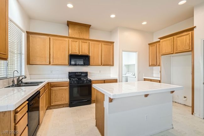 Kitchen with washing machine and dryer, black appliances, light floors, tile countertops, and a sink | Image 9