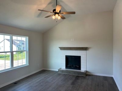 Unfurnished living room featuring ceiling fan, a tiled fireplace, vaulted ceiling, and dark hardwood / wood-style flooring | Image 2