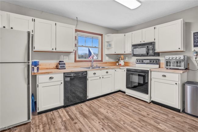 Kitchen featuring light countertops, black appliances, a sink, white cabinetry, and light wood-type flooring | Image 17