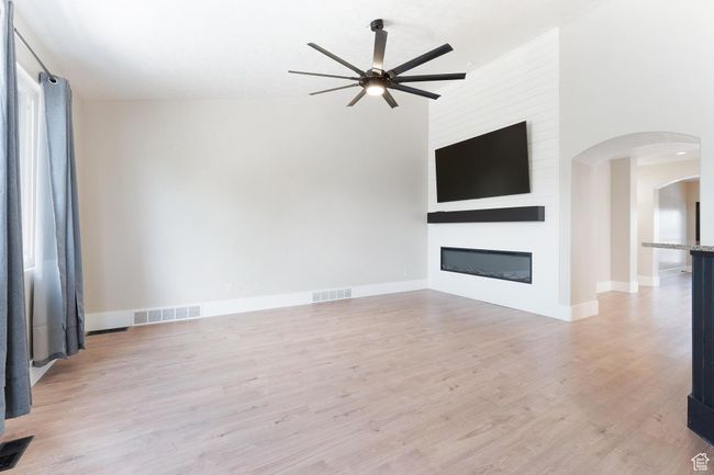 Great room with a vaulted ceiling, ceiling fan, arched walkways, light wood finished floors, and a large fireplace | Image 9