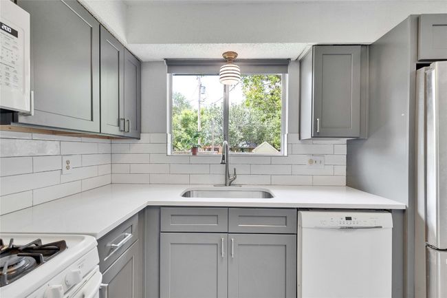 Kitchen with white appliances, gray cabinetry, light countertops, and tasteful backsplash | Image 13