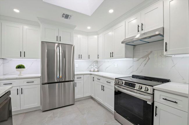 Kitchen with appliances with stainless steel finishes, under cabinet range hood, white cabinets, recessed lighting, and decorative backsplash | Image 4
