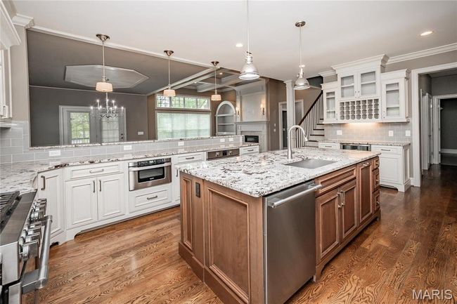 Kitchen featuring a sink, stainless steel appliances, glass insert cabinets, backsplash, and an island with sink | Image 11