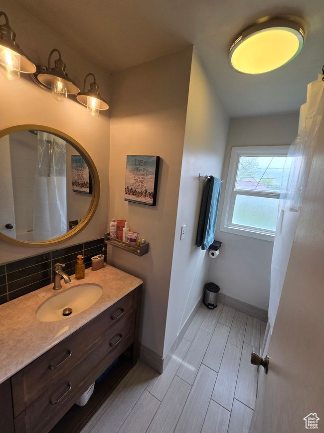Bathroom with tasteful backsplash, a shower with curtain, wood tiled floor, baseboards, and vanity | Image 28