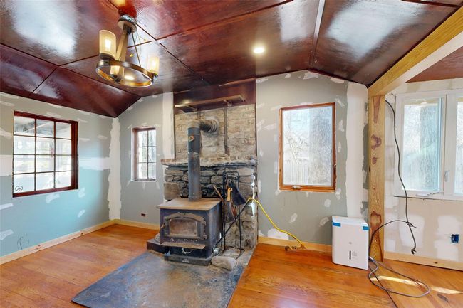 Living room with a chandelier, a wood stove, baseboards, wood-type flooring, and lofted ceiling | Image 7