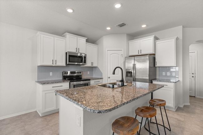 Kitchen, with stainless steel appliances, subway backsplash, Breakfast bar open to living room and white cabinetry with granite counter tops. | Image 9