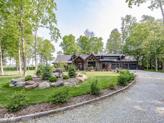 view of front of property featuring gravel driveway, stone siding, a front lawn, and a garage | Image 53