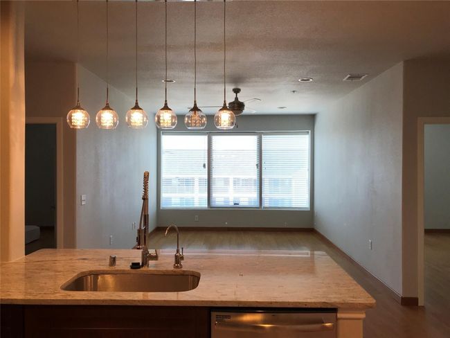 Kitchen with stainless steel dishwasher, wood finished floors, light stone counters, a sink, and hanging light fixtures | Image 9