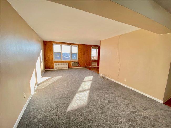 Carpeted empty room with radiator, wood walls, and an AC wall unit | Image 4