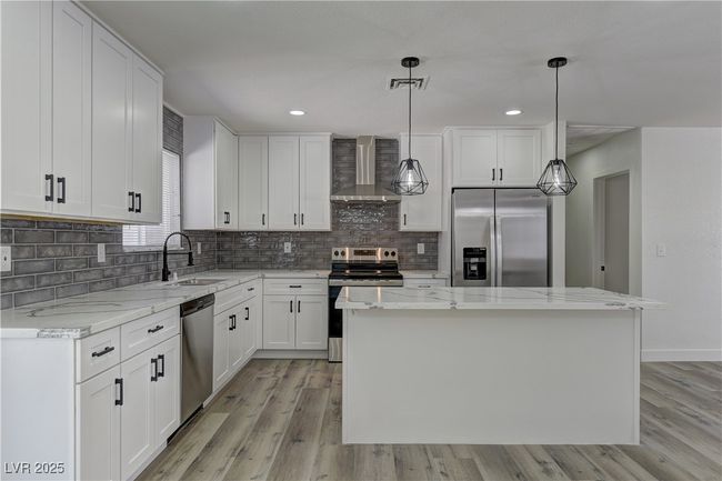 Kitchen featuring appliances with stainless steel finishes, wall chimney range hood, light wood-type flooring, tasteful backsplash, and a center island | Image 14