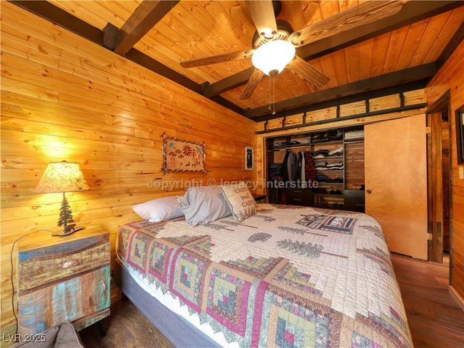 Bedroom with a closet, wood finished floors, beamed ceiling, wooden walls, and wooden ceiling | Image 18