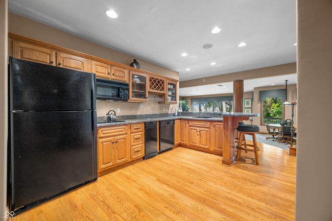 Bar kitchen featuring recessed lighting, glass insert cabinets, decorative columns, black appliances, and light wood-type flooring | Image 62