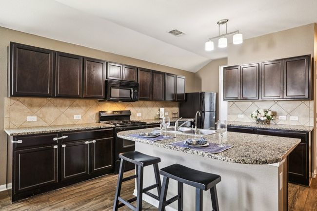 Kitchen with black appliances, dark wood-type flooring, lofted ceiling, a kitchen bar, and a center island with sink | Image 8