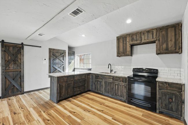 Kitchen featuring visible vents, black electric range oven, a sink, a barn door, and a peninsula | Image 15