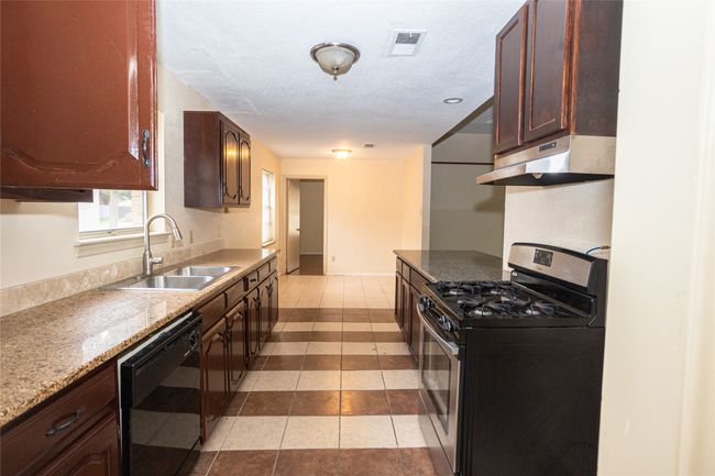 Kitchen with stainless steel range with gas cooktop, under cabinet range hood, dishwasher, light tile patterned floors, and granite countertops | Image 7