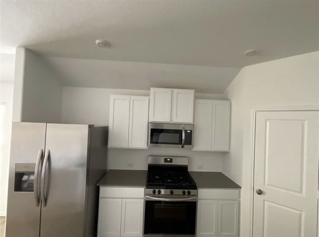 Kitchen featuring stainless steel appliances, lofted ceiling, white cabinetry, and dark countertops | Image 6