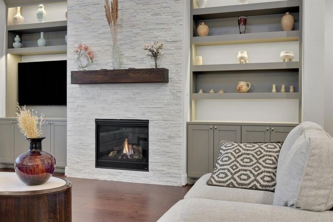 This inviting living room features a modern gas fireplace with mosaic stone surround and a dark wood mantel and built-in shelving. | Image 25
