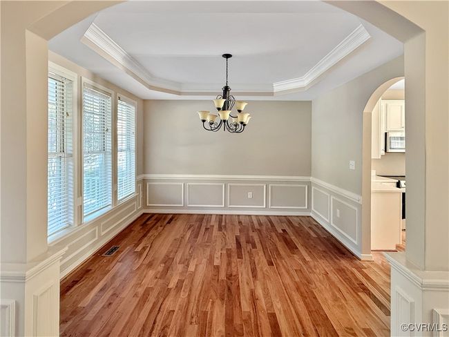 Unfurnished dining area featuring a tray ceiling, ornamental molding, light wood-type flooring, a chandelier, and a decorative wall | Image 4