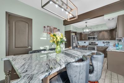 Kitchen featuring light stone countertops, a kitchen breakfast bar, stainless steel appliances, and tasteful backsplash | Image 1