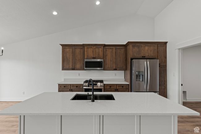 Kitchen featuring appliances with stainless steel finishes, lofted ceiling, a sink, light wood-style floors, and a kitchen island with sink | Image 6
