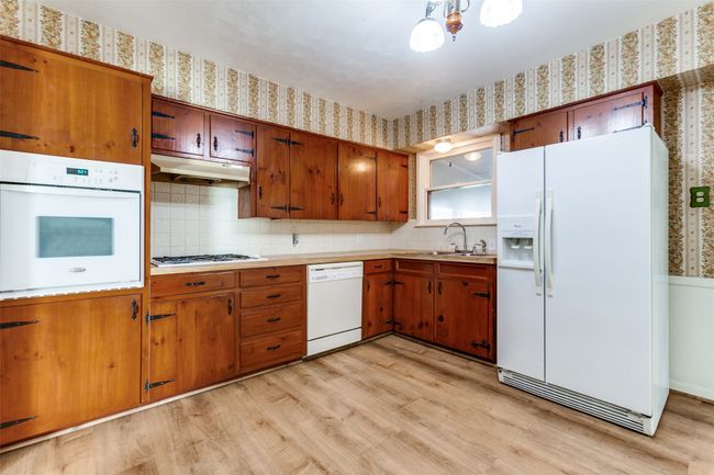 Kitchen featuring white appliances, wallpapered walls, under cabinet range hood, light wood-style flooring, and brown cabinetry | Image 6