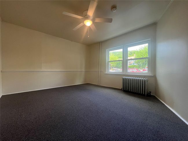 Empty room with radiator heating unit, a ceiling fan, dark colored carpet, a smoke detector, and baseboards | Image 12