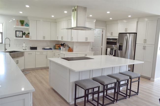 Kitchen featuring island exhaust hood, stainless steel appliances, a kitchen bar, a center island, and light wood-style flooring | Image 9