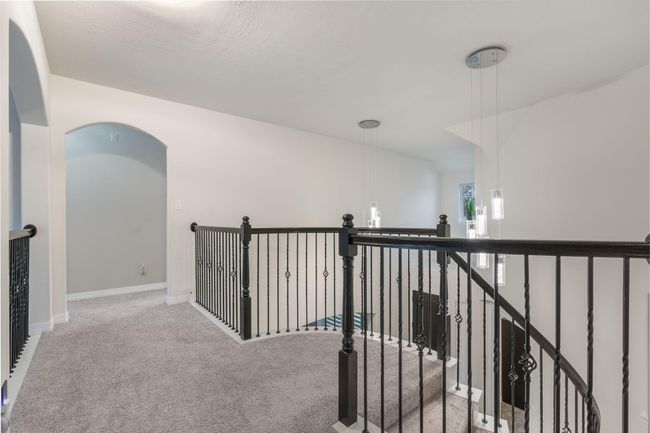 Carpeted upstairs hallway with elegant black wrought iron railings and stylish pendant lighting, leading to an arched doorway. | Image 26