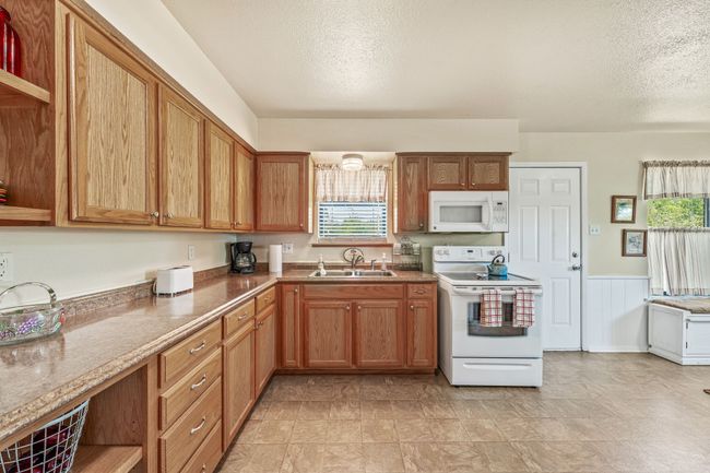 Kitchen with white appliances, a textured ceiling, open shelves, wainscoting, and a sink | Image 11