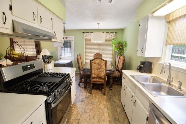 Kitchen with light countertops, appliances with stainless steel finishes, under cabinet range hood, a sink, and light wood-style floors | Image 8