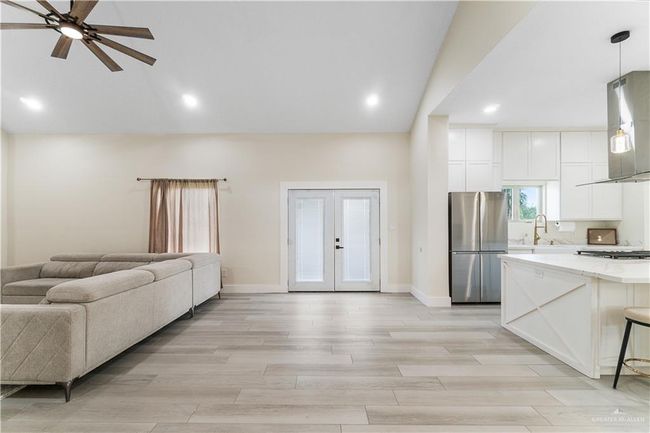 Kitchen with stainless steel refrigerator, decorative light fixtures, ceiling fan, a breakfast bar area, and white cabinets | Image 24