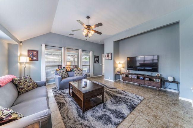 Tiled living area featuring a ceiling fan, vaulted ceiling, and baseboards | Image 4