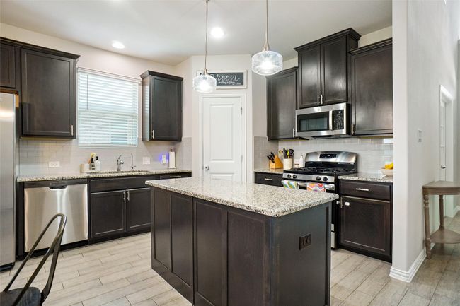 Kitchen with appliances with stainless steel finishes, light wood finished floors, a sink, a kitchen island, and light stone counters | Image 6