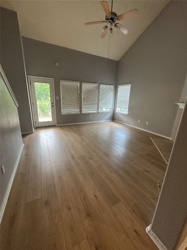 Empty room featuring high vaulted ceiling, a ceiling fan, wood finished floors, and baseboards | Image 12